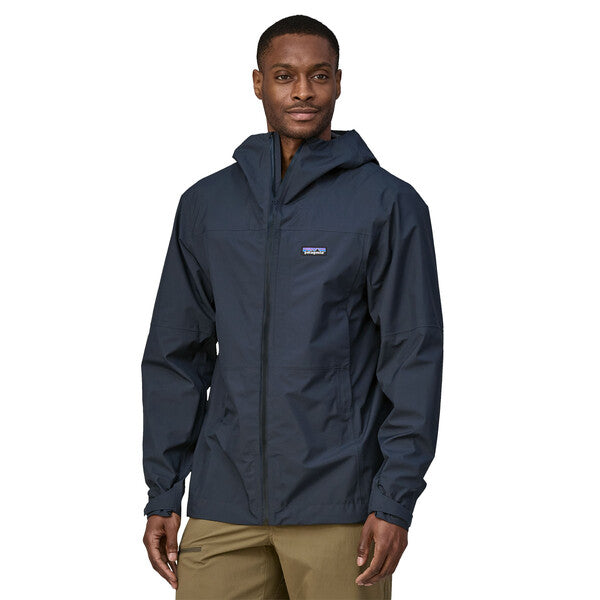 A man wearing a navy blue Patagonia men's boulder fork rain jacket with the hood down, standing against a plain background.
